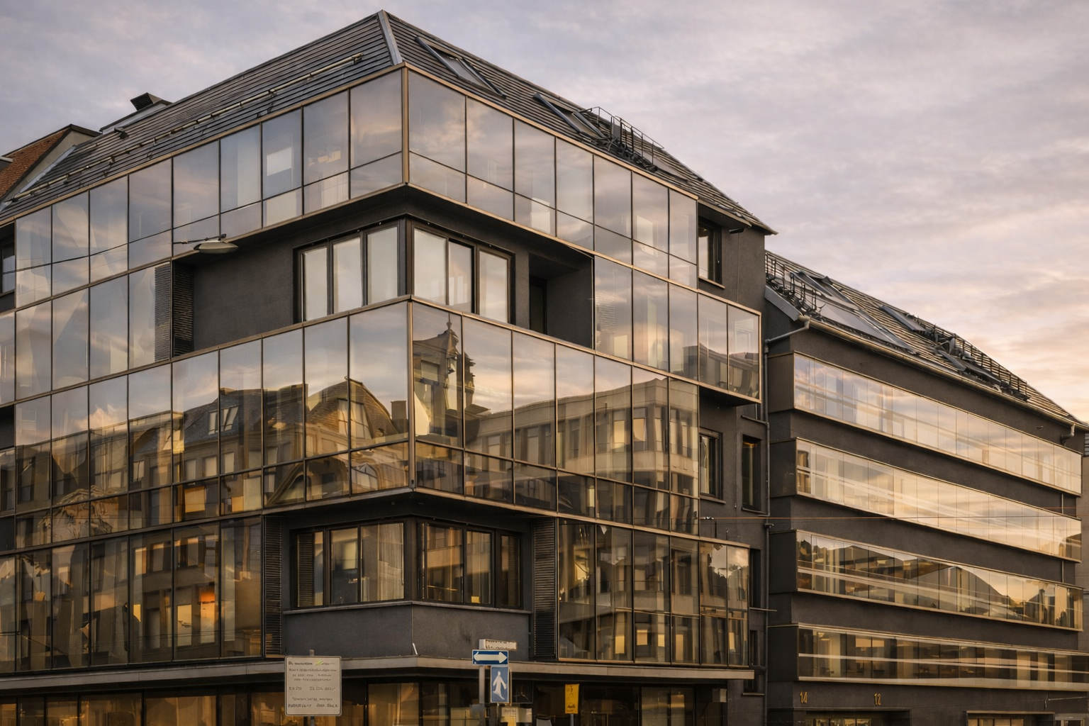 Eckgebäude mit Glasfassade und ausgebautem Dachgeschoss in der Abenddämmerung
